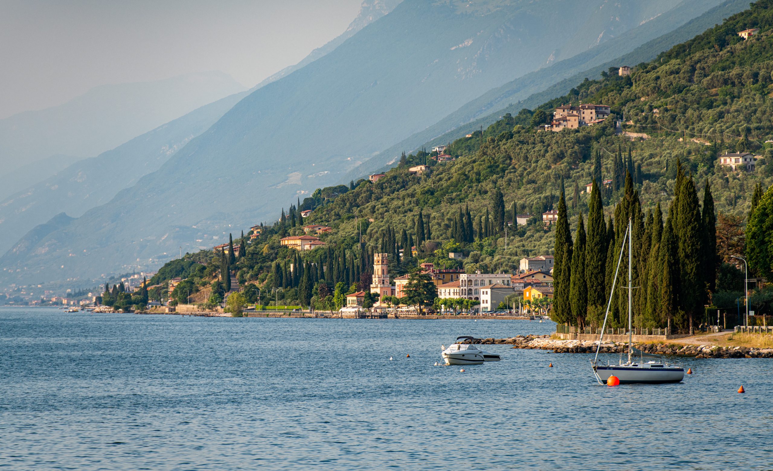 Boote liegen auf dem Gardasee, in Italien. Im Hintergrund ist der Turm von Pai (La Torre di Pai) zu sehen.