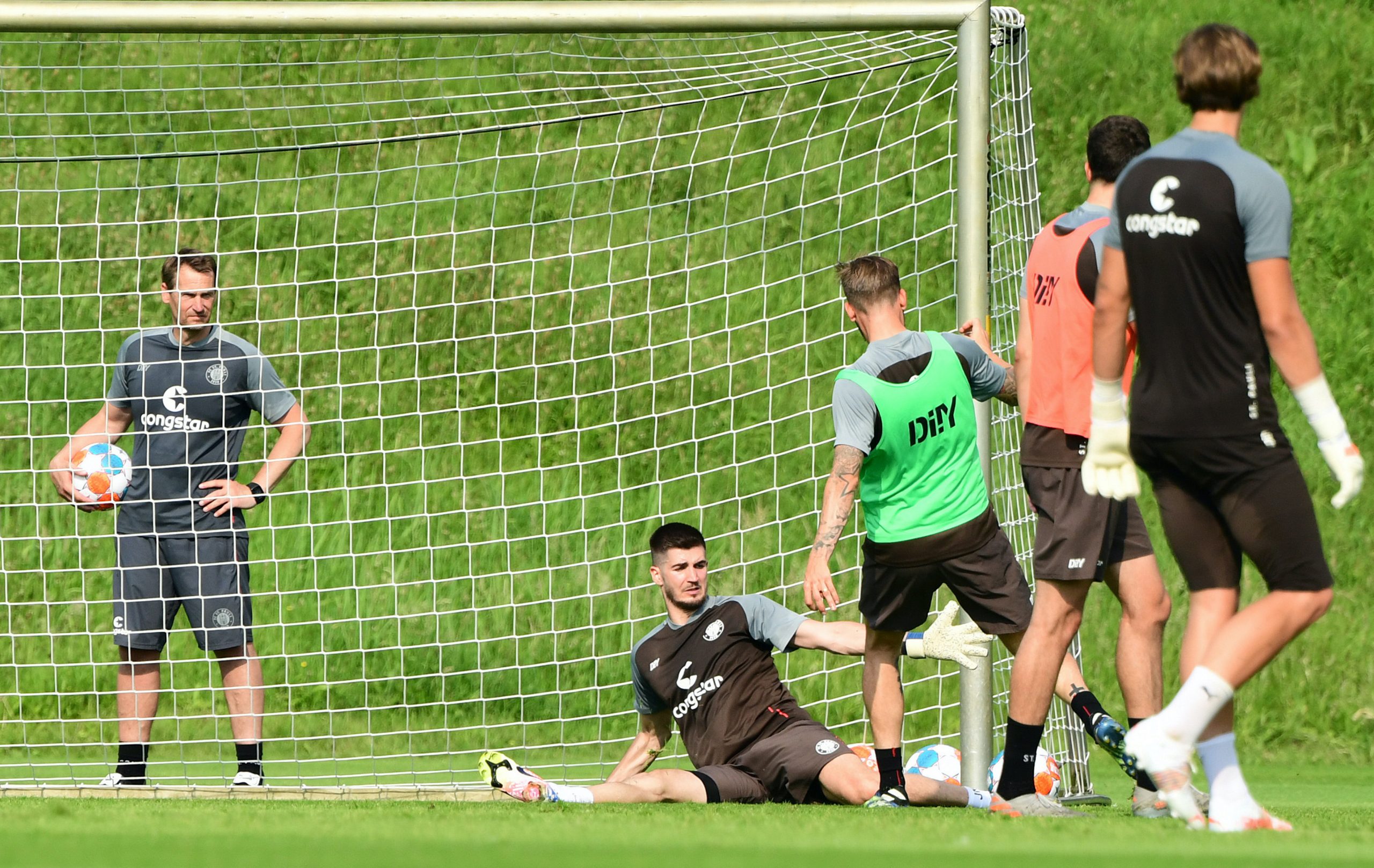 Keeper Nikola Vasilj (liegend) bekam bereits die Chance, sich zu beweisen – und allerlei Lob von Torwart-Trainer Mathias Hain (l.).