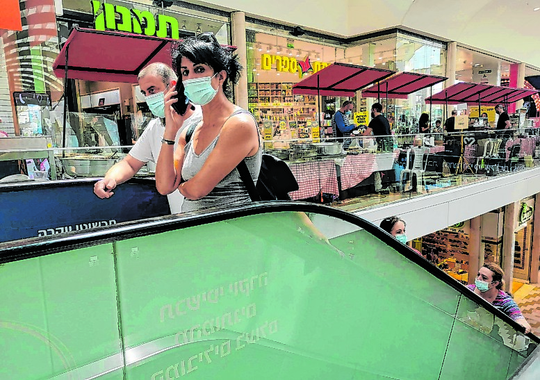 Zwei Menschen fahren mit Maske auf einer Rolltreppe in einem israelischen Einkaufszentrum