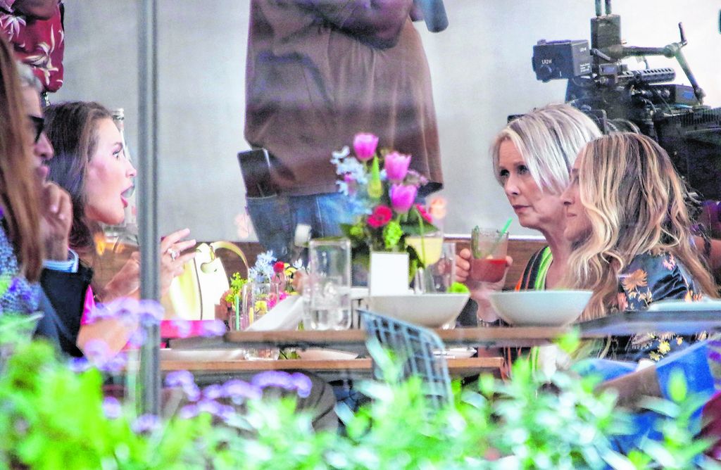 Die Schauspielerinnen Carrie, Charlotte und Samantha sitzen und plaudern gemeinsam beim Essen