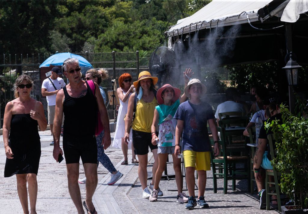 Passanten in Athen kühlen sich am Sprühnebel eines Straßencafés ab.