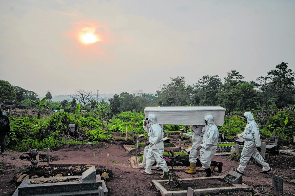 Friedhofsmitarbeiter in Schutzkleidung tragen einen Sarg über einen Friedhof in Indonesien.