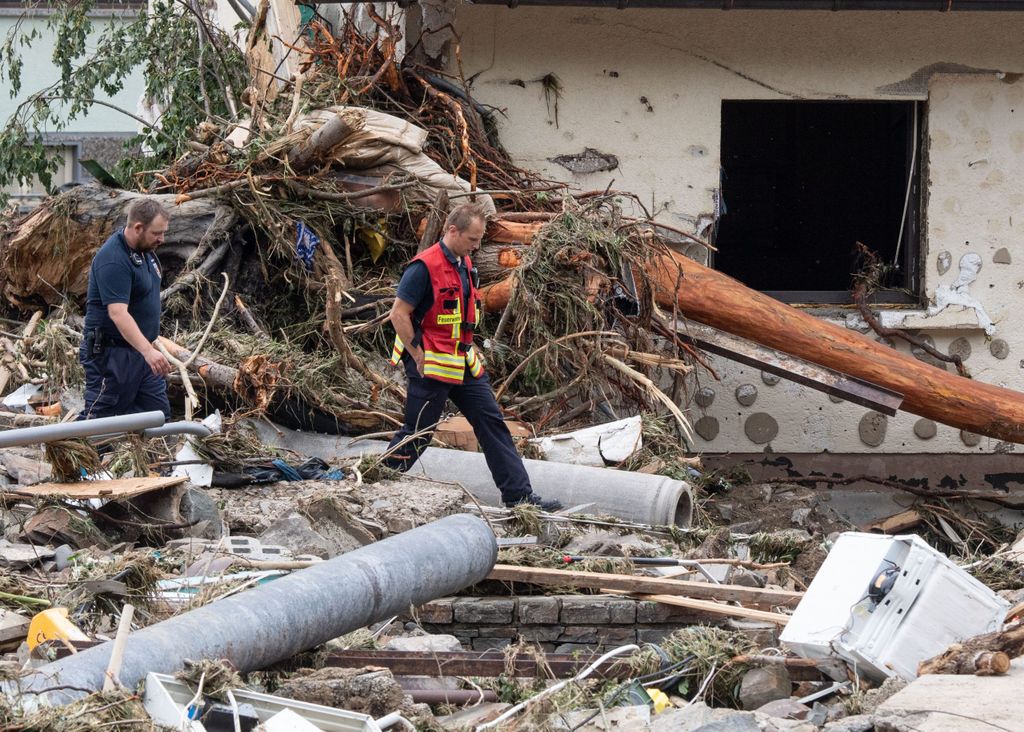 Zwei Feuerwehrleute gehen in dem Dorf im Kreis Ahrweiler nach dem Unwetter mit Hochwasser durch den Schutt. Mindestens sechs Häuser wurden durch die Fluten zerstört.