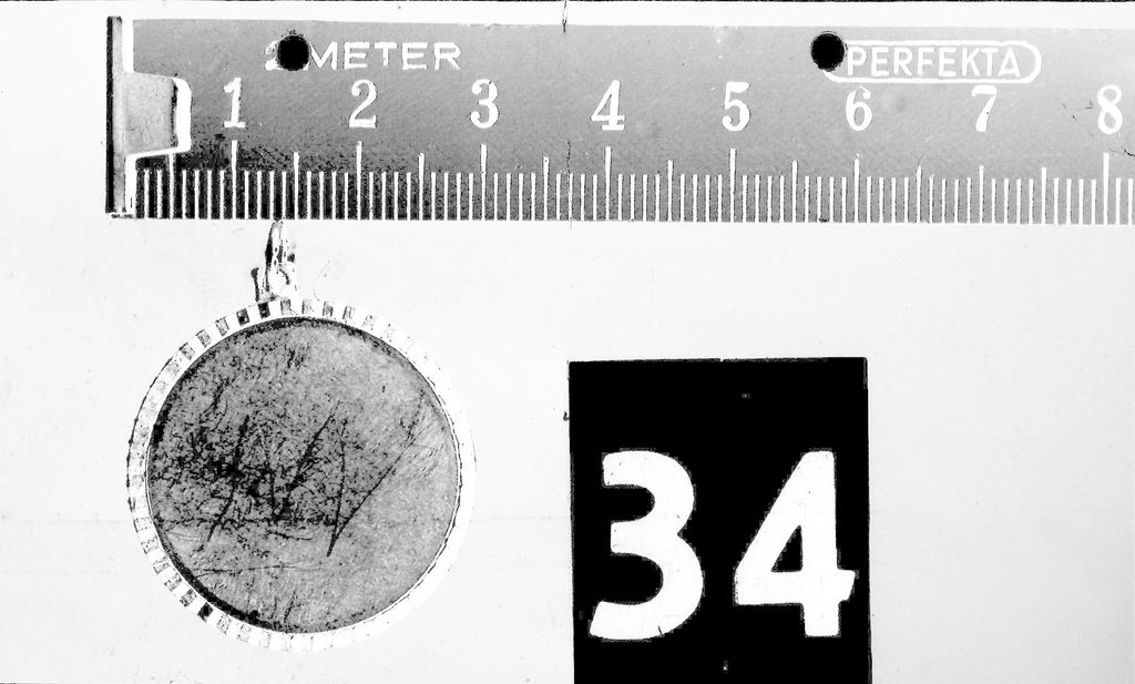 Der Anhänger einer Kette, die am Tatort gefunden wurde. Bei den eingeritzten Buchstaben könnte es sich um ein „M“ und ein „V“ handeln.