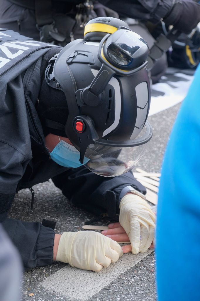 Ein Polizist benutzt einen speziellen Stoff, um die festgeklebten Hände vom Asphalt zu lösen.