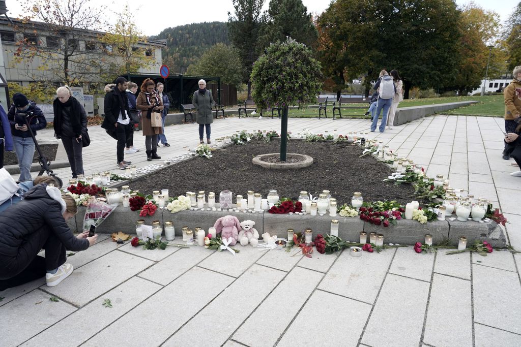 Personen stehen vor Blumen, Kerzen und Kuscheltiere, die in Gedenken an die Opfer niedergelegt wurden.