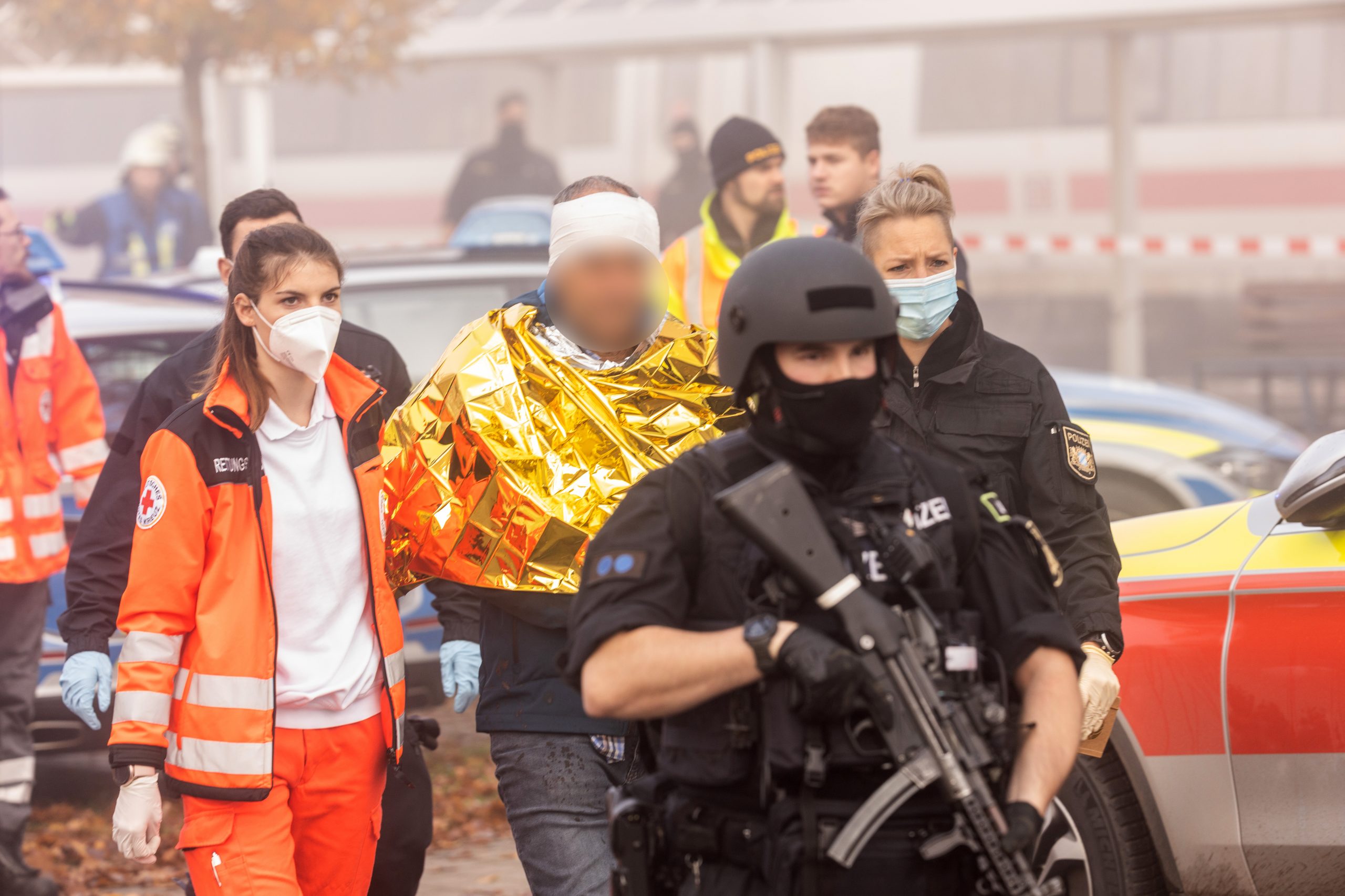 Eine festgenommene männliche Person wird am Bahnhof von Polizei und Rettungskräften weggeführt.