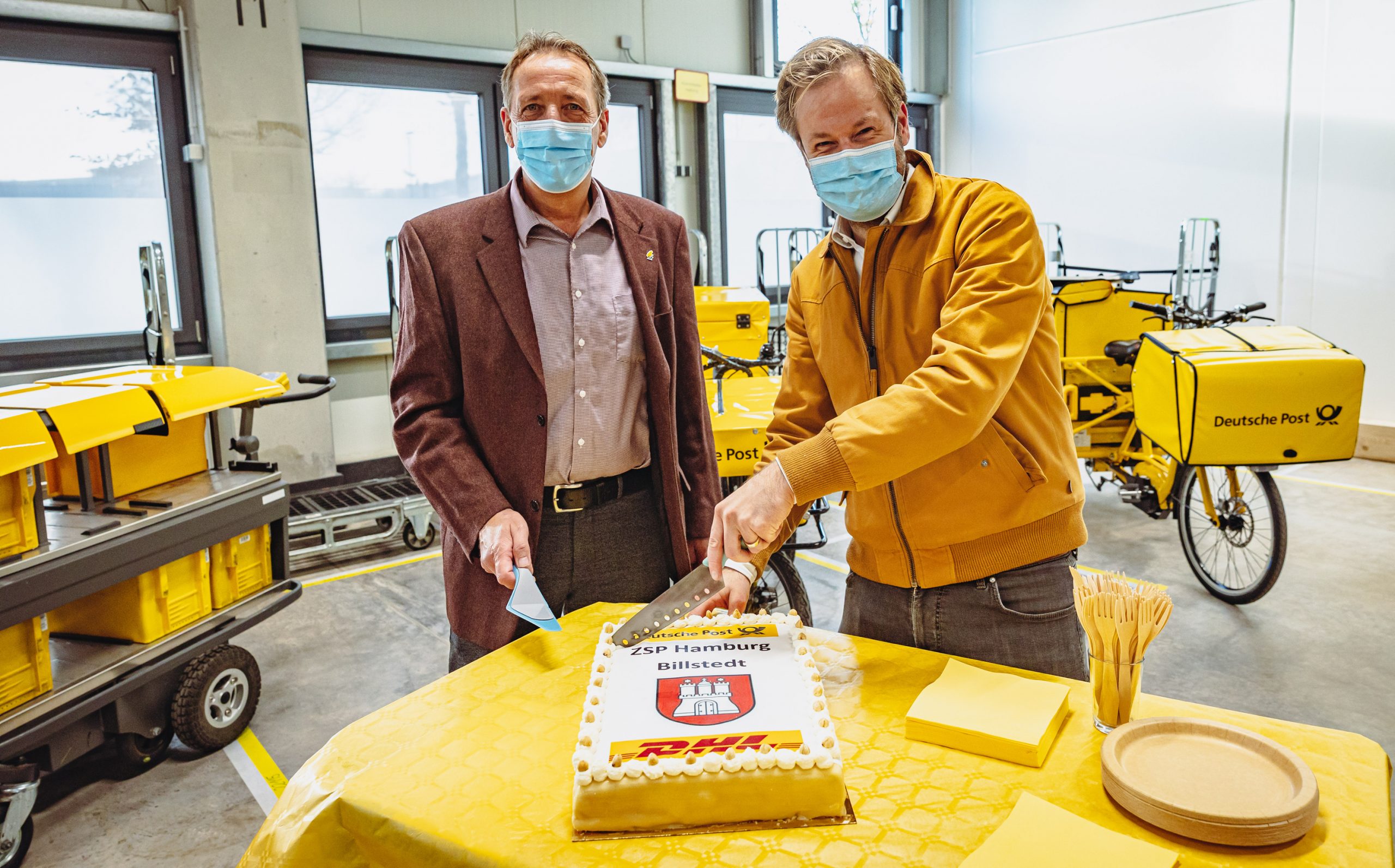 Verkehrssenator Anjes Tjarks (re)) und Niederlassungsleiter Stefan Eckelmann schneiden eine Torte an